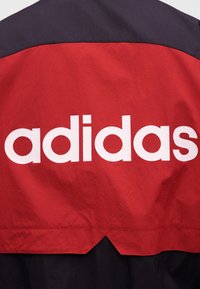 Červená a černá tkanina s velkým bílým textem "adidas" vytištěným přes střed červené části materiálu.