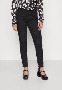 Černé kalhoty s žebrovanou texturou na předních stehnech, dokončené se slim fit střihem. Spárované s vzorovanou blůzou a lesklými botami na blokovém podpatku.