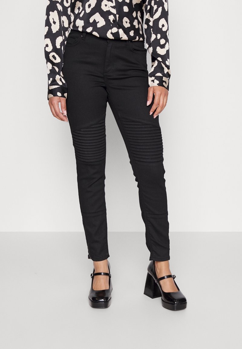 Černé kalhoty s žebrovanou texturou na předních stehnech, dokončené se slim fit střihem. Spárované s vzorovanou blůzou a lesklými botami na blokovém podpatku.