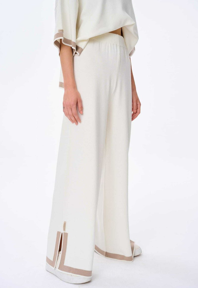Losse, beige-accentueerde, lichtgewicht broeken van een gestructureerde witte stof met zijsplitten aan de zoom voor ventilatie.