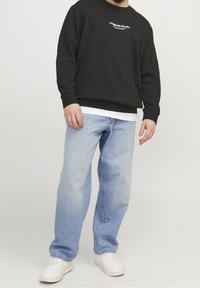 Felpa nera con logo bianco, abbinata a jeans dritti azzurri chiari. Sneakers bianche completano l'outfit.