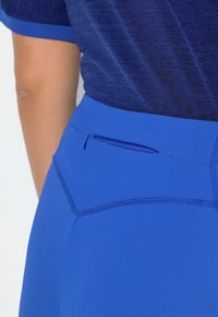 Niebieskie legginsy sportowe o fakturowanym wykończeniu, z zamykaną na zamek kieszenią, wysokim stanem oraz kontrastującymi przeszyciami wzdłuż szwów.