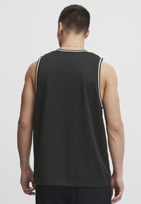 Sort atletisk tanktop med netstruktur, der har en rund halsudskæring og hvid accentsting på ærmegab og krave.