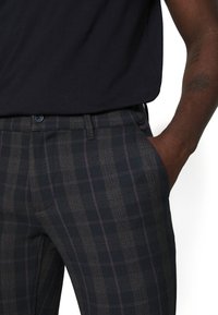 Slim-fit rutiga byxor med mörka nyanser och lila accenter, knappstängning och sidofickor i ett texturerat tyg.