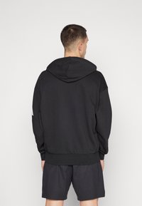 Black hooded sweatshirt with long sleeves, ribbed cuffs, and hem. Features a solid design and relaxed fit, paired with dark shorts.