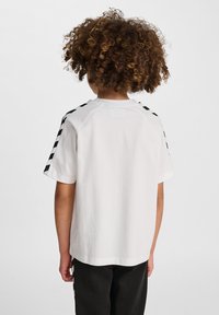 T-shirt blanc avec des rayures en damier noir sur les épaules. Manches courtes et coupe décontractée. Matière en coton doux.