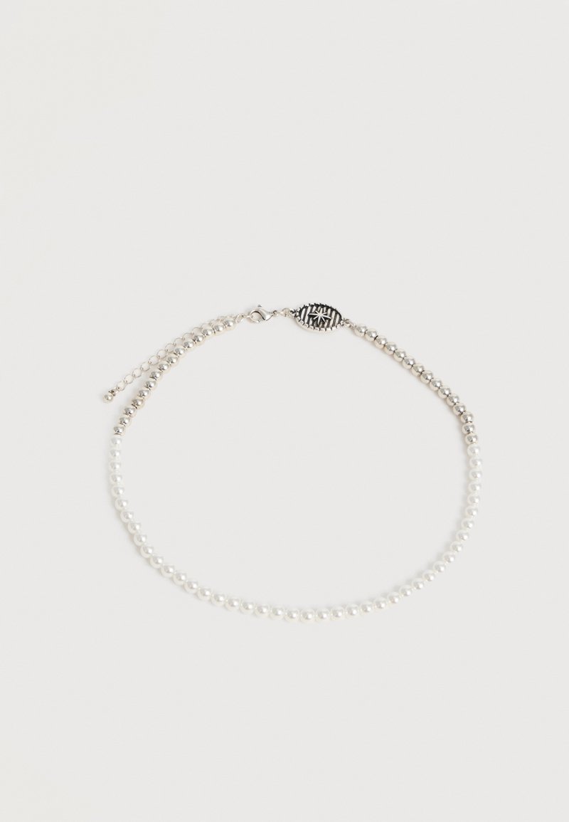 Bracelet perlé argenté et blanc avec chaîne ajustable et fermoir ovale présentant un motif étoile sur fond blanc uni.