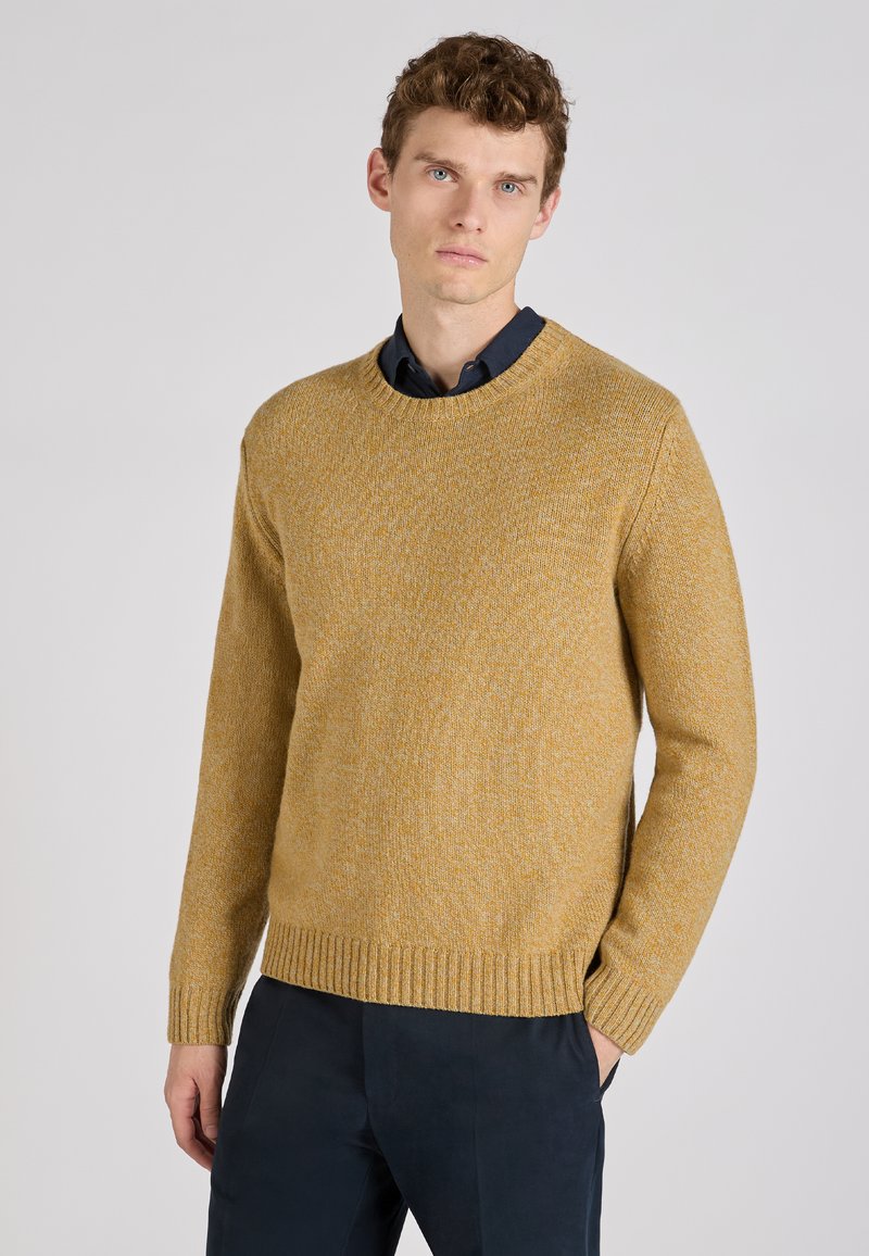 Pull en tricot jaune avec une finition texturée, col rond, poignets et ourlet côtelés, assorti à une chemise à boutons foncée et un pantalon bleu marine.
