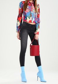 Blusa corta de flores multicolores, jeans ajustados negros y botas de tobillo azul cielo. Bolso cilindrico rojo con asa.