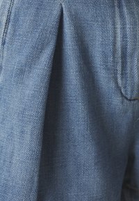 Svetlo moder denim material z teksturirano površino in nabranimi detajli, s šivi ob robovih in subtilnim leskom.