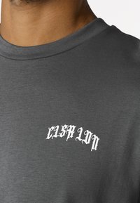 Dunkelgraues T-Shirt mit Rundhalsausschnitt, getragen von einer Person, mit weißem, gotischem Schriftzug "EISPLIN" auf der oberen Brust.