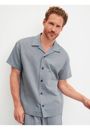 Kurzärmeliges Hemd mit Knöpfen aus hellgrauem, strukturiertem Stoff, mit Camp-Kragen und dunklen Knöpfen, getragen mit locker sitzender passender Hose.