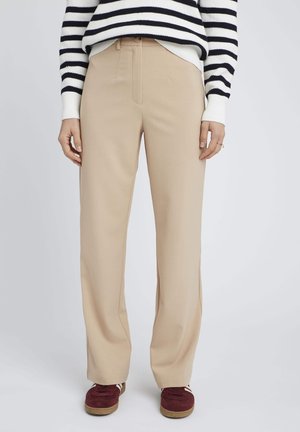 Pantalons beige à jambes larges avec une texture lisse et un léger éclat, dotés d'une taille ajustée et d'un ourlet droit, associés à des baskets bourgogne.