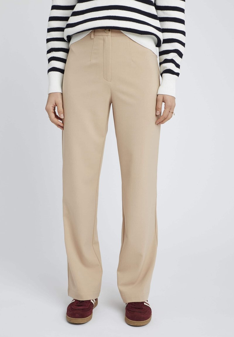 Pantalons beige à jambes larges avec une texture lisse et un léger éclat, dotés d'une taille ajustée et d'un ourlet droit, associés à des baskets bourgogne.
