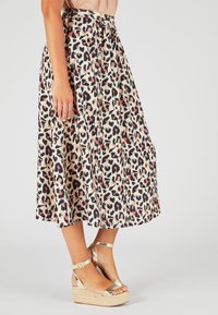 Falda midi de estampado de leopardo en beige, con manchas negras y naranjas. Tejido ligero con diseño plisado y cintura. Cuñas de esparto doradas.