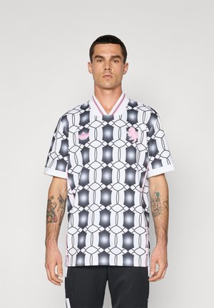 Jersey blanco de manga corta con un patrón geométrico en negro y rosa, con escote en V y ribete de color contrastante en el cuello. Logo de la marca deportiva en el pecho.