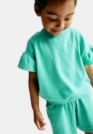 Kortekous, mintgroene outfit gemaakt van gestructureerde stof, met ruffles aan de mouwen en shorts met elastische taille.