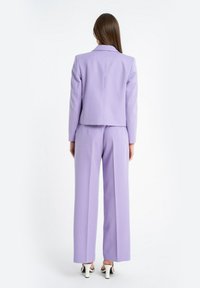 Fioletowa marynarka o dopasowanym kroju i szerokie spodnie. Gładki materiał, dopasowana góra i luźne spodnie o prostym kroju. Szpilki mają kontrastujący akcent.