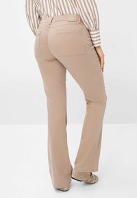Beige Gerade-Hosen mit glatter Textur, ausgestattet mit Gesäßtaschen und einem Logotag am Bund, kombiniert mit einem gestreiften Oberteil und flachen Schuhen.