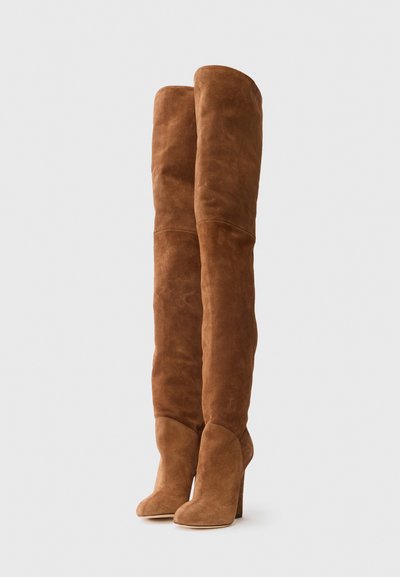 Botas de ante marrón por encima de la rodilla con un diseño elegante, punteras puntiagudas y tacones gruesos. Presentan líneas verticales suaves y una textura suave.