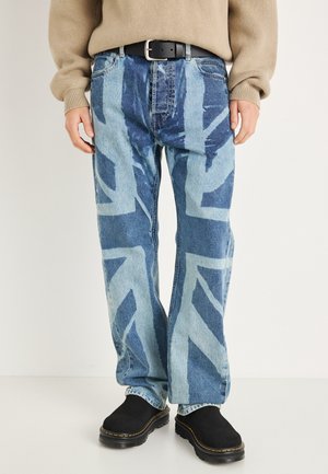 Jean en denim bleu clair avec un motif audacieux du drapeau Union Jack en bleu foncé. Le jean a une coupe décontractée et est associé à des chaussures noires sans lacets.