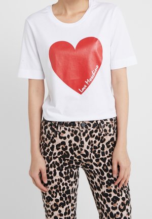 Wit t-shirt met grote rode hart en tekst "Love Moschino", gecombineerd met hooggetailleerde broek met luipaardprint, gedragen door een persoon die staat.