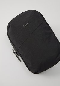Sac à dos noir en tissu résistant, avec une texture lisse, une fermeture éclair et un petit logo métallique Nike à l'avant.