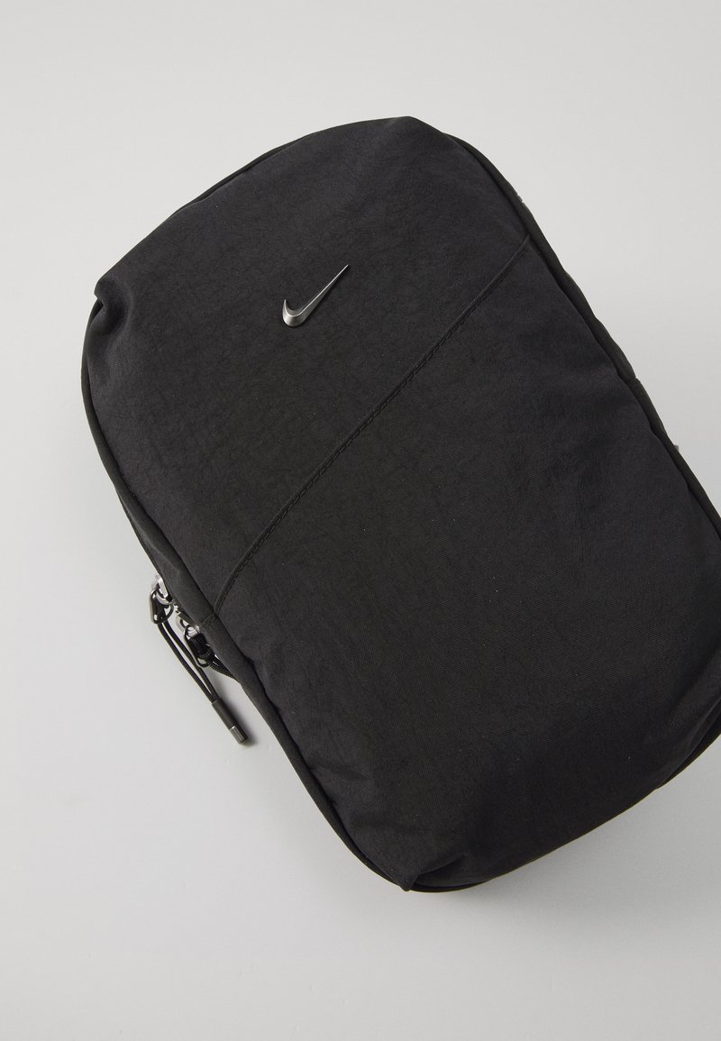 Schwarzer Rucksack aus strapazierfähigem Stoff, mit glatter Textur, Reißverschluss und einem kleinen metallischen Nike-Logo auf der Vorderseite.