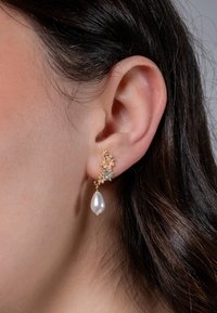 Gold earrings featuring small floral accents with gemstones and a large teardrop-shaped pearl. The design is delicate and intricate.