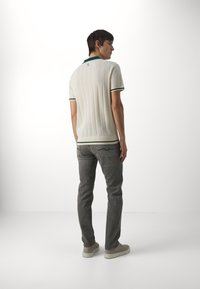 Polo in maglia a maniche corte da uomo, di colore crema con accenti verdi, abbinato a jeans grigi. La camicia presenta una texture a coste e un design aderente.