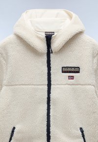 Beige fleece jacket with a soft, textured surface, front zipper, and navy accents. Features logo patch and two zippered side pockets.