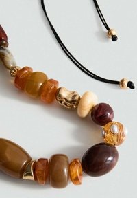 Collier en perles avec des perles de différentes tailles en ambre, marron et doré, sur un cordon noir et avec des accents dorés. Finitions lisses et texturées.