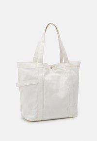 Canvas tote bag i off-white med två axelremmar, två sid sömmar och en sidficka. Har kontrasterande sömnad och en tryckknappsstängning.