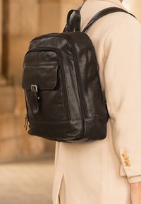 Must must seljakott esipocketi ja reguleeritavate rihmadega, millel on sile tekstuur ja minimalistlik disain.