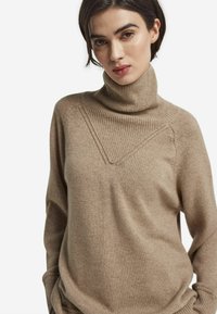 Beige polotröja i mjukt stickat material. Har en ribbad krage och en V-formad detalj på bröstet med avslappnad passform.