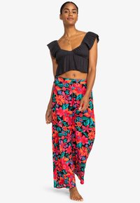 Čierny volánkový crop top spárovaný s farebnými palazzo nohavicami s kvetinovým vzorom, ktoré obsahujú červené a ružové kvety na čiernom pozadí.