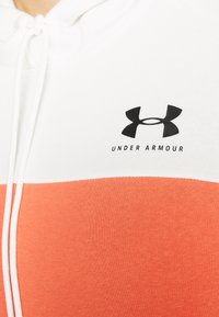 Sudadera con capucha que tiene una sección superior blanca y una sección inferior naranja. Presenta un logo negro de "Under Armour" en el pecho. Mezcla de algodón.