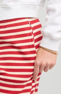 Red and cream striped ribbed skirt with a fitted shape, paired with a white long-sleeve sweater and a gold chain bracelet on the wrist.