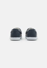 Marineblaue Lederschuhe mit niedrigem Profil, weißen Gummisohlen und dekorativer Naht. Mit silbernen Ösen für die Schnürsenkel.
