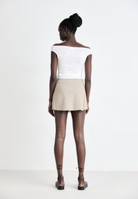 Hvid off-shoulder top parret med en beige mini nederdel. Modellen bærer strappy sorte sandaler. Glat tekstur, moderne design.