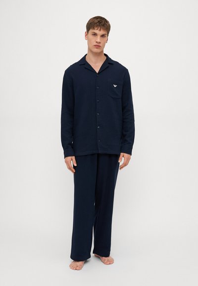 Navy blauwe pyjama set met een knoopsluiting shirt met een borstzak en losse pasvorm broek, gemaakt van een zachte, gestructureerde stof.