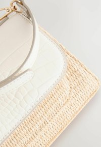 Borsa in ecopelle bianca con base in paglia naturale intrecciata. Presenta una trama ripetuta e un manico solido.
