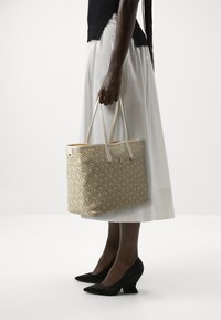 Borsa a spalla color sabbia con una trama intrecciata e un motivo di piccoli accenti blu e oro. Presenta lunghe maniglie bianche e un interno arancione in contrasto.