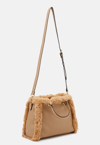 Borsa in pelle color cuoio con bordo in pelliccia soffice, accessori in oro, manici corti e una lunga tracolla regolabile appesa su uno sfondo bianco.