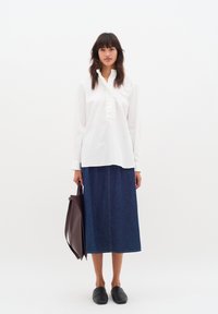 Vit långärmad skjorta med volangdetaljer, kombinerat med en mörk denim-midi kjol, svarta slip-on skor och en vinröd tygväska.