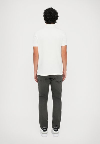 Camisa polo branca de mangas curtas, corte standard, combinada com jeans cinzentos e sapatilhas brancas com pormenores pretos. Design simples e limpo.