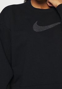 Sweatshirt noir avec un logo Nike texturé et pailleté sur la poitrine. Le tissu est doux avec une finition lisse et un col rond.