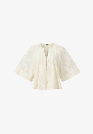 Chemisier en dentelle couleur crème avec manches larges arrivant au coude, motif floral, encolure ronde et fermeture à boutons sur le devant.