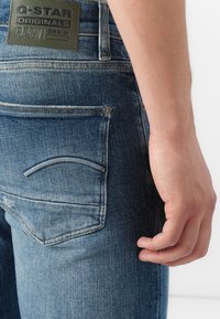 Los vaqueros de G-Star RAW presentan un color azul desgastado, un parche de cuero de la marca en la parte trasera y un diseño de bolsillo curvado.