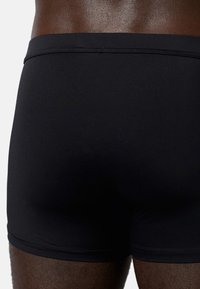Schwarze Badeshorts mit glatter Textur, ausgestattet mit einer tief sitzenden Taille und dezenten Nähten. Entworfen für eine enganliegende Silhouette.